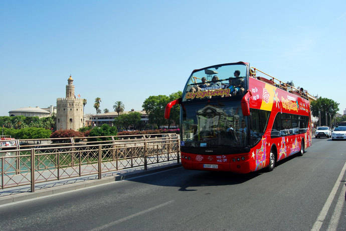 Un autobús de City Sightseeing con la Torre del Oro al fondo.